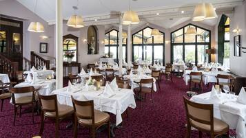 A dining area with multiple tables set for service, large windows, and a staircase leading to an upper level.
