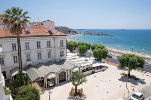 A hotel with a terrace, palm trees, and a view of the beach and sea.