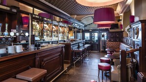 A bar with wooden bar counters, stools, and a seating area with cushioned chairs and tables. - Excelsior (Saint-Raphael)