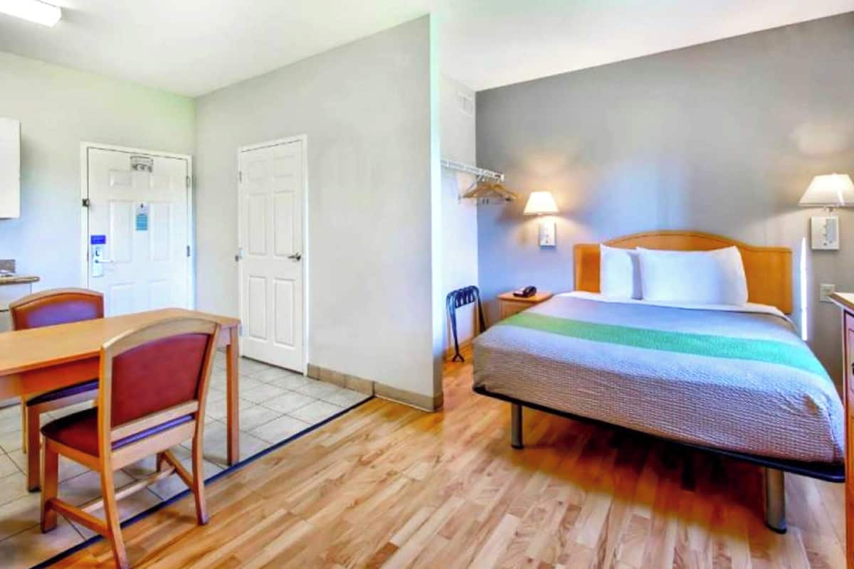 Una camera d'albergo con un letto, un comodino, una lampada e una sedia.