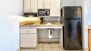 A compact kitchen with white cabinets, a stainless steel refrigerator, a microwave, and a sink with a visible pipe. - Oyo Townhouse Sulphur,LA Extended Stay I-10 (Sulphur)