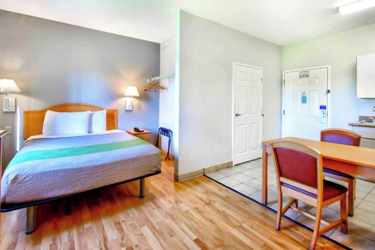 Camera d'albergo con un letto, comodino, lampada e un tavolino con sedie.