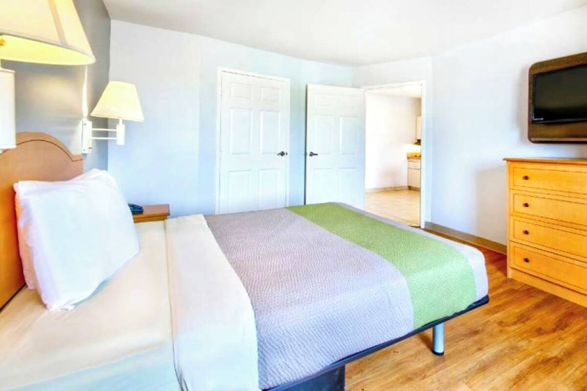 Camera d'albergo con un letto, una cassettiera in legno, una televisione e due porte che danno su altre stanze.