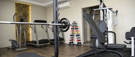 Un gimnasio con una prensa de banca, una estructura para sentadillas y un estante de pesas montado en la pared.
