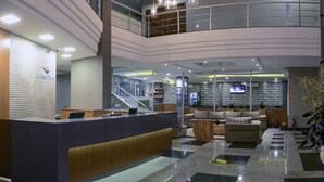 Un vestíbulo de hotel con recepción, zona de estar, escalera y una gran planta en maceta.