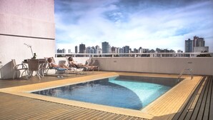 Piscina en la azotea con sillones de descanso y vistas a un horizonte urbano.