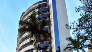 Un hotel moderno de varios pisos con fachada curva, balcones y palmeras.