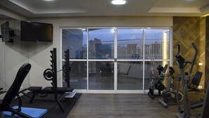 Un gimnasio con equipo de ejercicio, un televisor y un amplio ventanal que da a un espacio exterior.