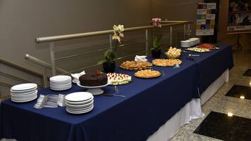 A buffet table with various desserts and plates, set against a wall with a railing and a poster.