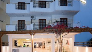 Un edificio de varios pisos con balcones, una entrada cubierta y un árbol con flores rosadas.