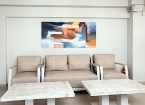 Una sala de estar moderna con un sofá color beige, dos mesas de centro blancas y un cuadro abstracto grande en la pared.