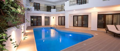 A multi-level indoor swimming pool with a tiled floor, surrounded by balconies and windows.