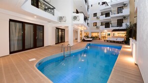 Piscina interior moderna con suelo de baldosas, rodeada de balcones y una zona de comedor con mesas al aire libre.