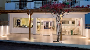 Un edificio moderno con un espacio exterior cubierto, amplias ventanas y un árbol de flores rosadas.