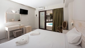 Habitación de hotel con cama, escritorio, silla, televisor y puerta corrediza hacia una zona de piscina.