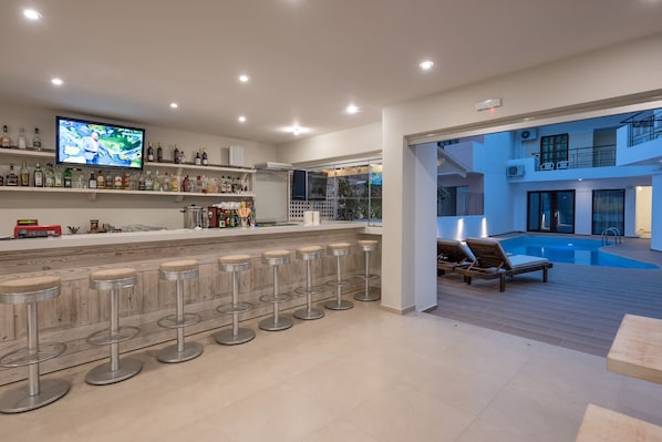 Un área de bar moderna con una zona de estar junto a la piscina y un televisor montado en la pared.