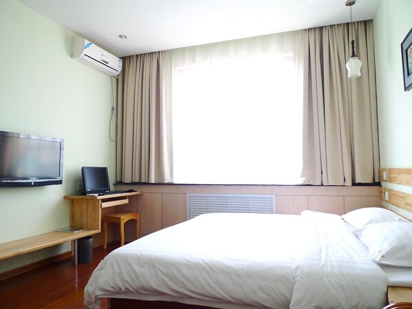Une chambre d’hôtel avec un lit, un bureau avec un ordinateur portable, un téléviseur fixé au mur et une fenêtre avec des rideaux.