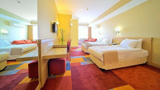 A hotel room with two beds, a small table, a chair, and a colorful carpet. - SV Business Hotel Diyarbakır (Diyarbakir)