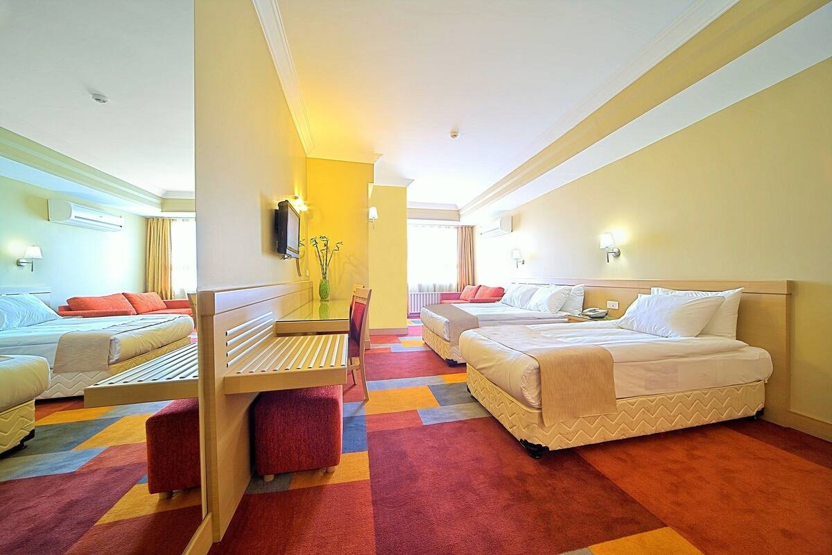 A hotel room with two beds, a small table, a chair, and a colorful carpet.