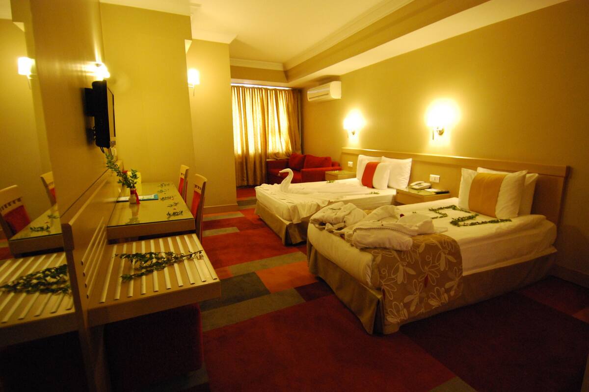 A hotel room with two beds, a desk, a mirror, and a window with curtains.