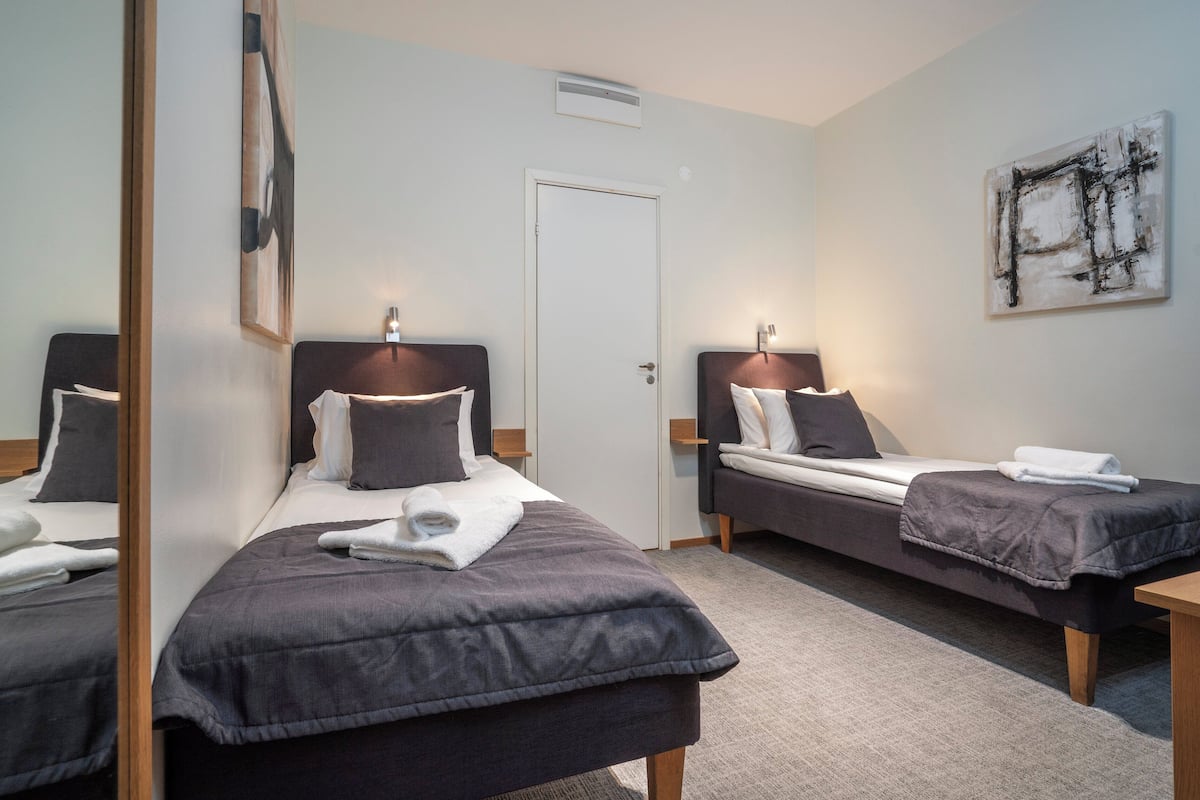 A hotel room with two single beds, a door, a wall-mounted artwork, and a small table.