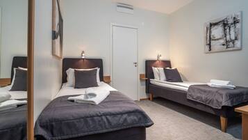 A hotel room with two single beds, a door, a wall-mounted artwork, and a small table.