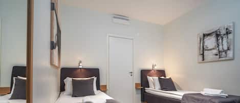 Habitación de hotel con dos camas individuales, una puerta, una obra de arte colgada en la pared y una pequeña mesa.