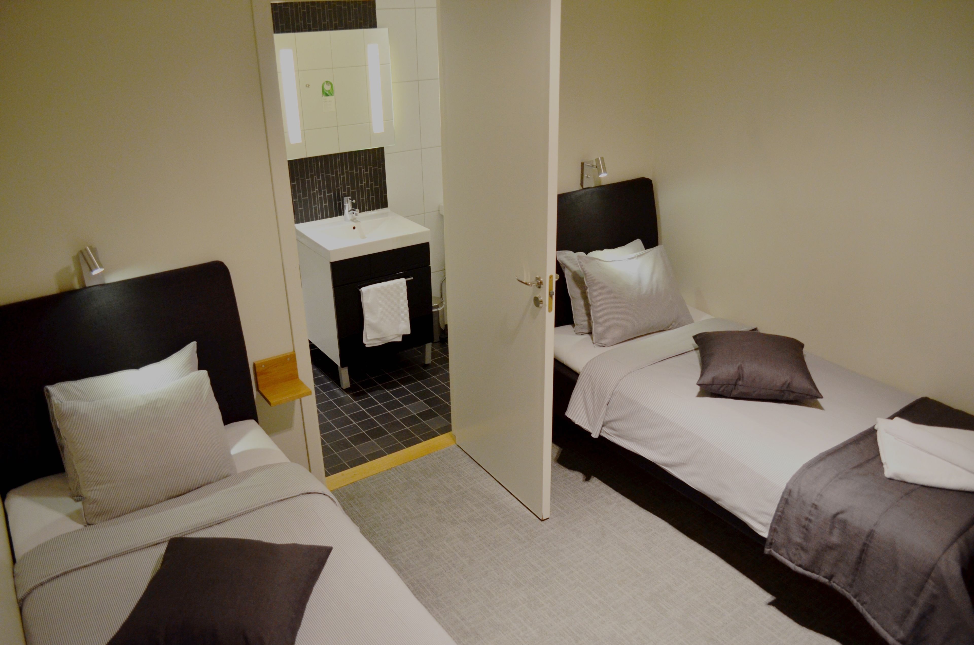 Habitación de hotel con dos camas, baño y una pequeña zona de estar.