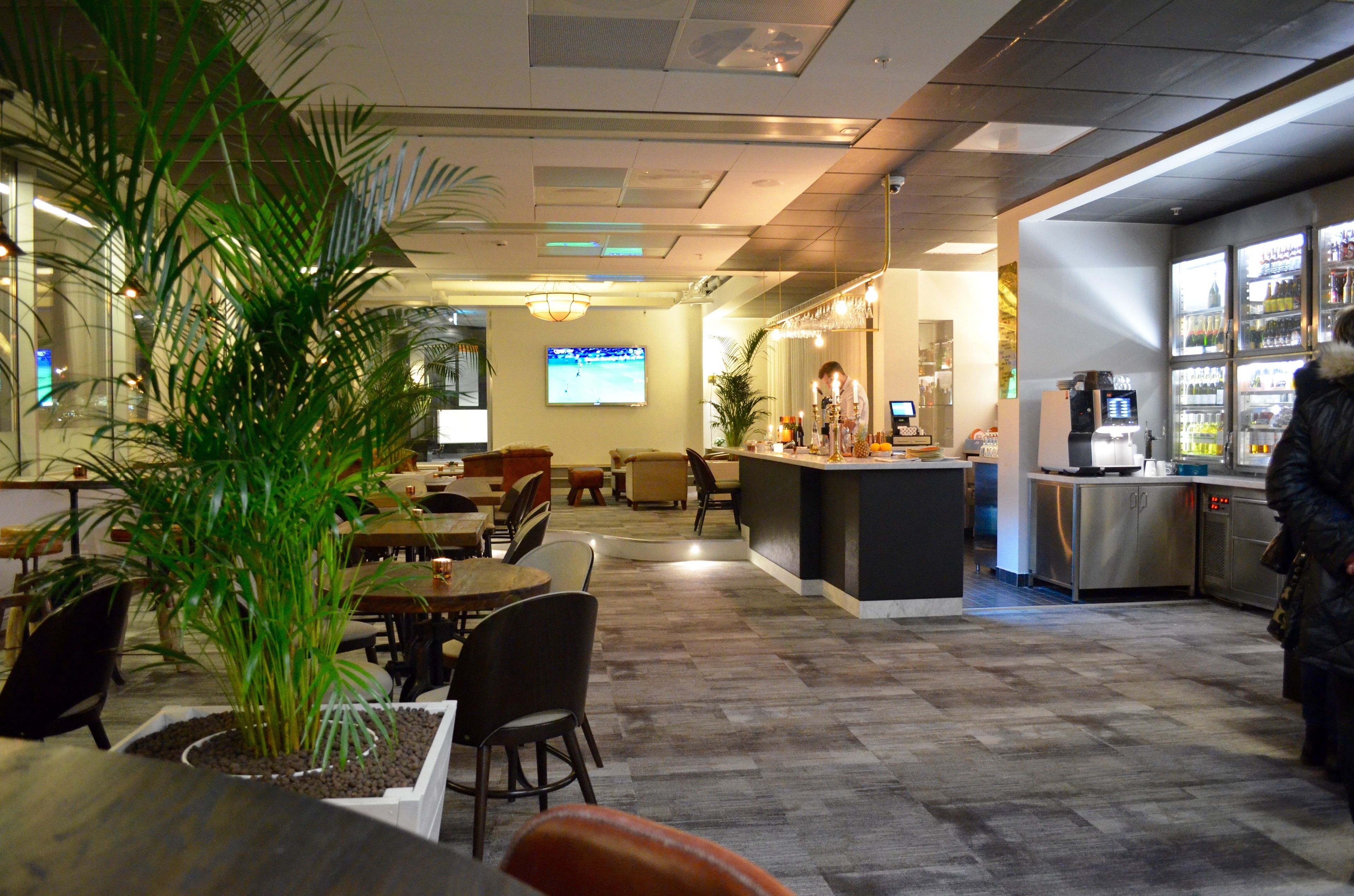 A modern hotel lobby with a seating area, a bar, and a television screen.