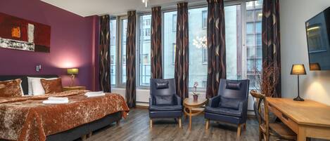 A modern hotel room with a large bed, two armchairs, a small table, and a desk.