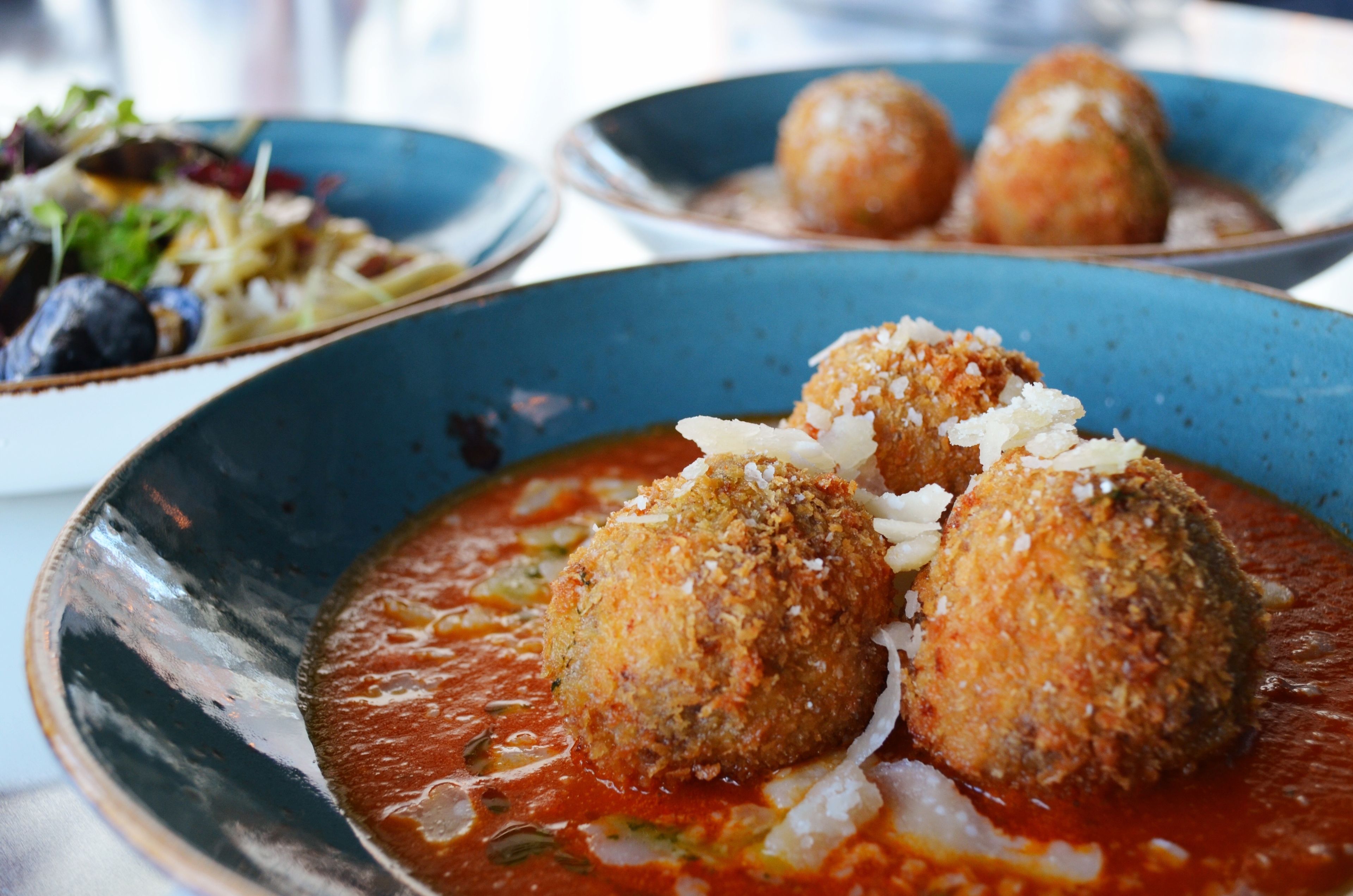 Een bord met daop drieklauwige gehaktballetjes in tomatensaus, bestrooid met geraspte kaas.