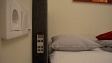 A hotel room with a control panel, a bed with pillows, and a wall-mounted air conditioning unit.
