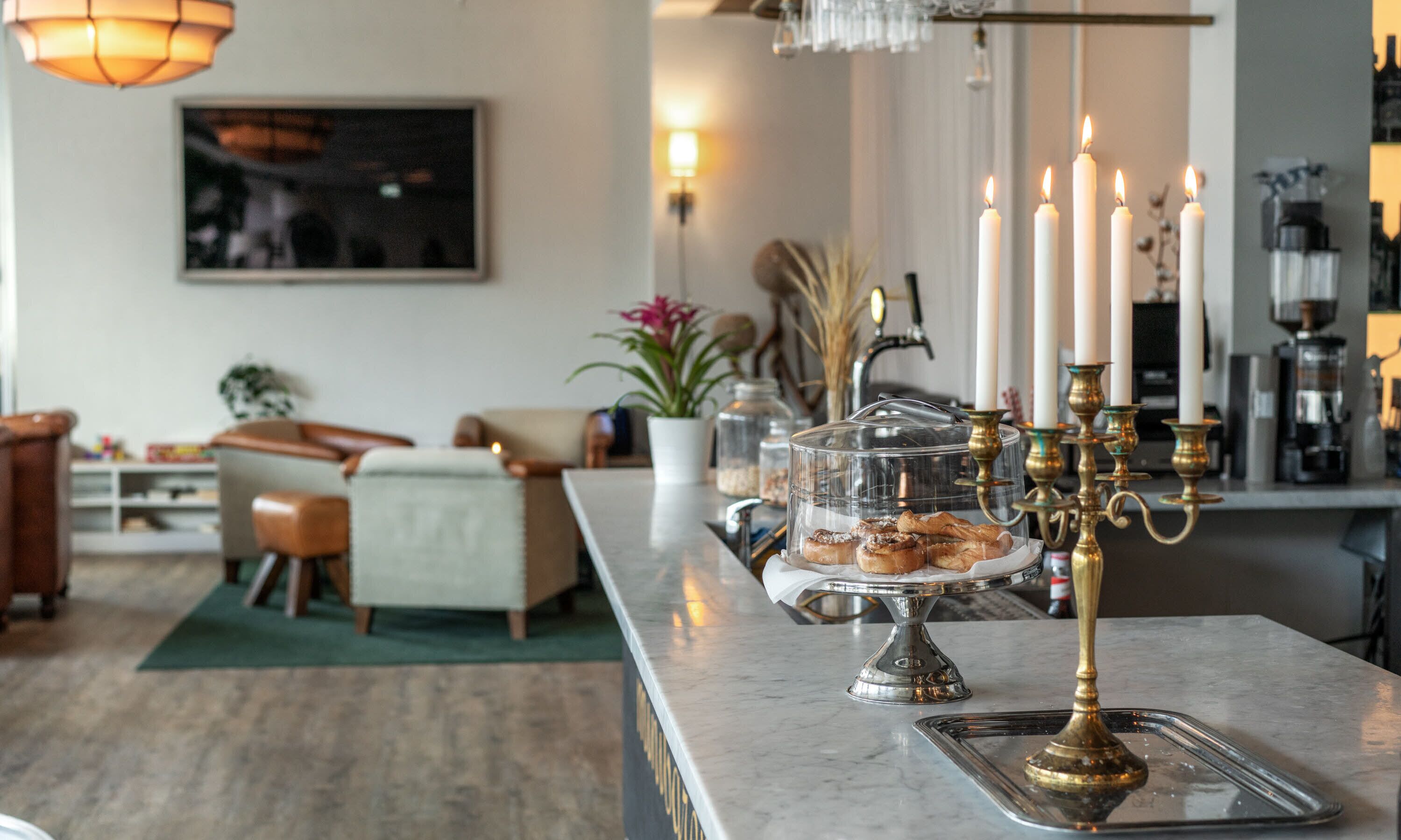 Eine Marmorbar mit einer Glastheke voller Gebäck, einem Kerzenleuchter mit brennenden Kerzen und einer Kaffeemaschine im Hintergrund.
