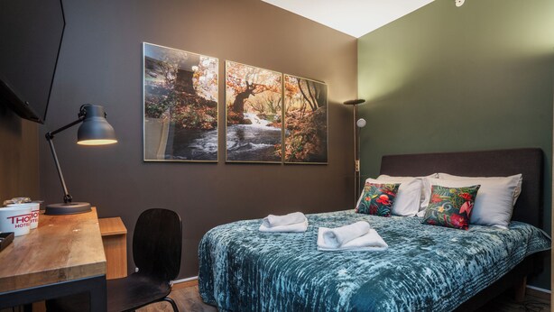 Une chambre à coucher avec un lit, un bureau, une chaise et une lampe de bureau. Trois tableaux encadrés sont accrochés au mur.
