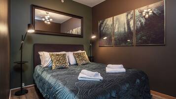 A bedroom with a large bed, two bedside lamps, a mirror, and a forest-themed wall art.