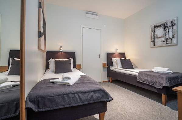 A hotel room with two single beds, each with a bedside table and lamp, a door, and a large abstract painting on the wall.