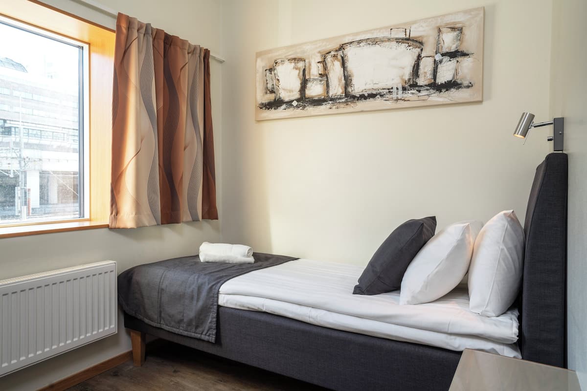 A bedroom with a bed, a radiator, a window with curtains, and a painting on the wall.