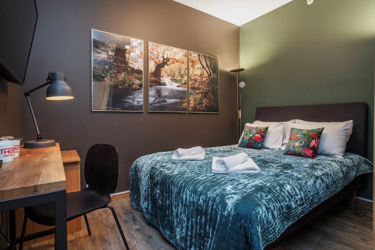 A bedroom with a bed, a desk, a chair, and a desk lamp.