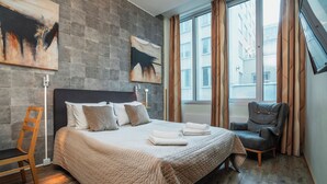 Hotellihuone, jossa on suuri sänky, tuoli ja taideteoksia seinillä.