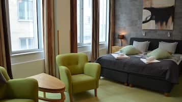 Habitación de hotel con cama, dos sillas, una mesa y ventana con cortinas.