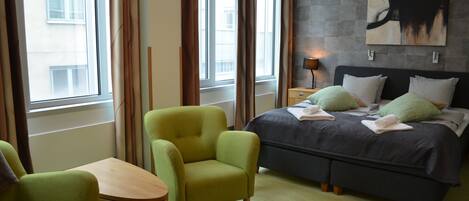 A hotel room with a bed, two chairs, a table, and a window with curtains.