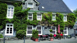 A building with a sign reading "Hotel zur Post" and outdoor seating with red umbrellas. - Hotel Gräfrather Hof (Solingen)
