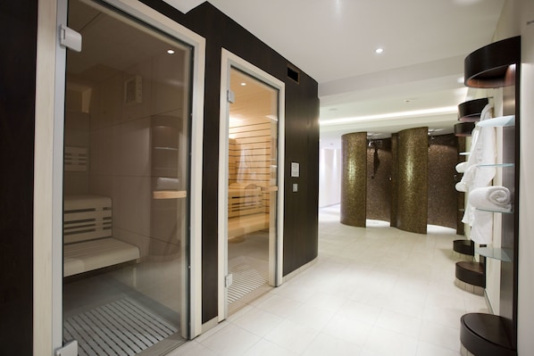 A modern hotel bathroom with a walk-in shower, glass shelves with towels, and a wooden bench.