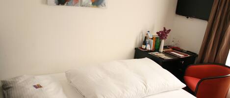Habitación de hotel con cama, un escritorio con silla, televisor de pantalla plana y arte abstracto en la pared.