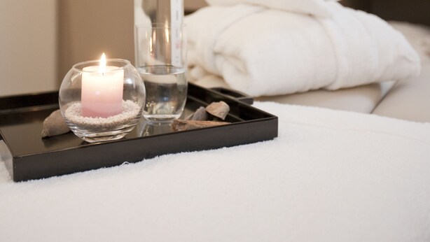 A neatly arranged bathroom with a white towel, a glass bottle, and a lit candle on a tray. - Hotel Gräfrather Hof (Solingen)