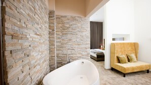A modern bathroom with a freestanding bathtub, stone walls, and a yellow armchair. - Hotel Gräfrather Hof (Solingen)