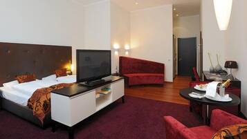 Ein Hotelzimmer mit einem Bett, einem Fernseher auf einer weißen Kommode, einem roten Sofa, einem kleinen Esstisch und einem Spiegel.