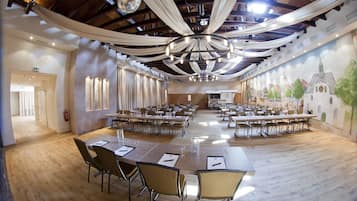 Una gran sala de conferències amb taules llargues i cadires, un lampadari i un mural a la paret.