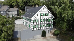 A traditional half-timbered house with multiple windows and a sloped roof, surrounded by trees and other houses. - Hotel Gräfrather Hof (Solingen)