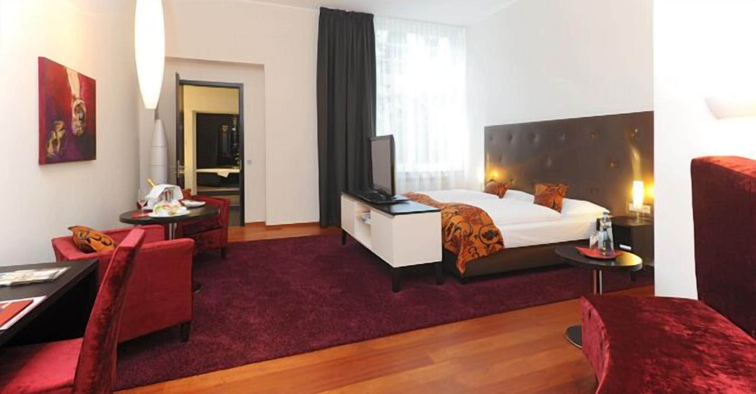 Ein Hotelzimmer mit Bett, Schreibtisch, Stuhl, Fernseher und einem fenster mit Vorhängen.